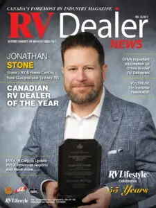 A man in a navy suit holds a glass award plaque, standing in front of a magazine cover titled "RV Dealer News" with the headline "Canadian RV Dealer of the Year.