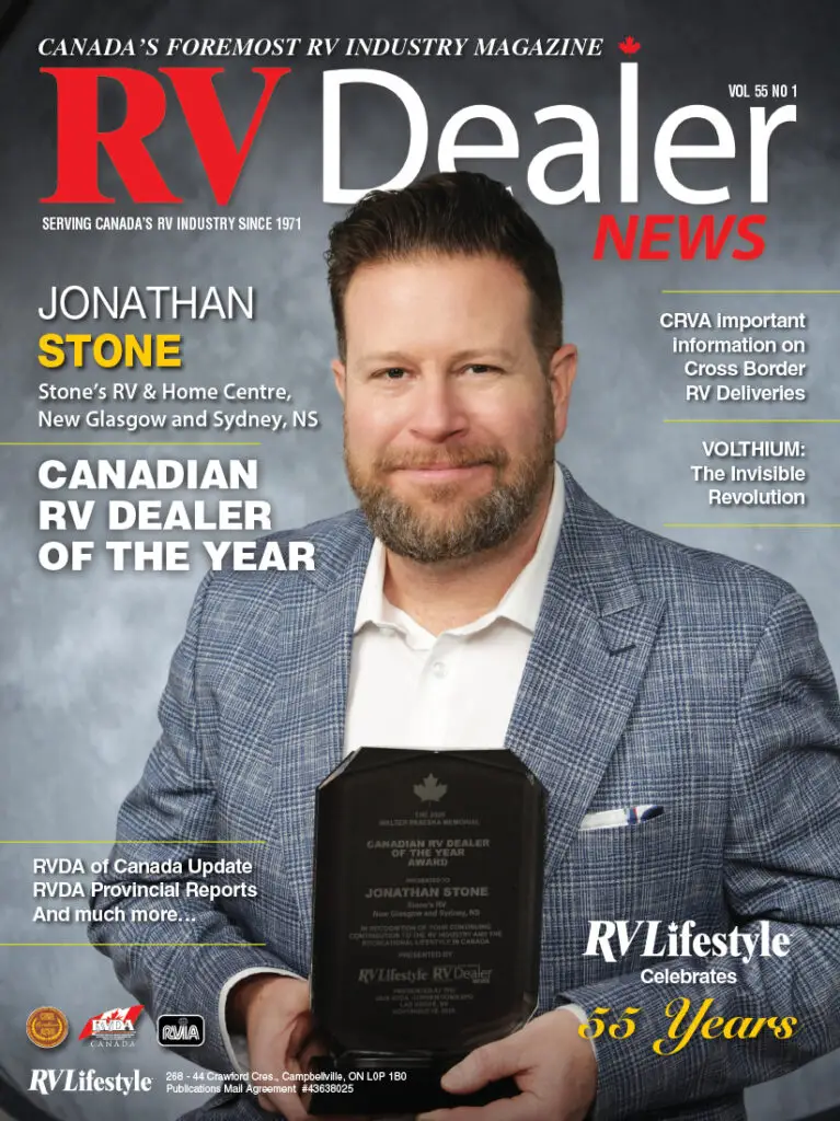 A man in a navy suit holds a glass award plaque, standing in front of a magazine cover titled "RV Dealer News" with the headline "Canadian RV Dealer of the Year.