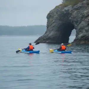 Two kayakers in life jackets paddle on calm coastal water near a rocky tidal sea cave in Annapolis, Nova Scotia.