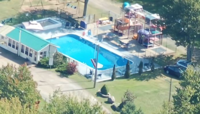 A backyard with a rectangular swimming pool, a swing set, and a large playground structure surrounded by trees and grass.